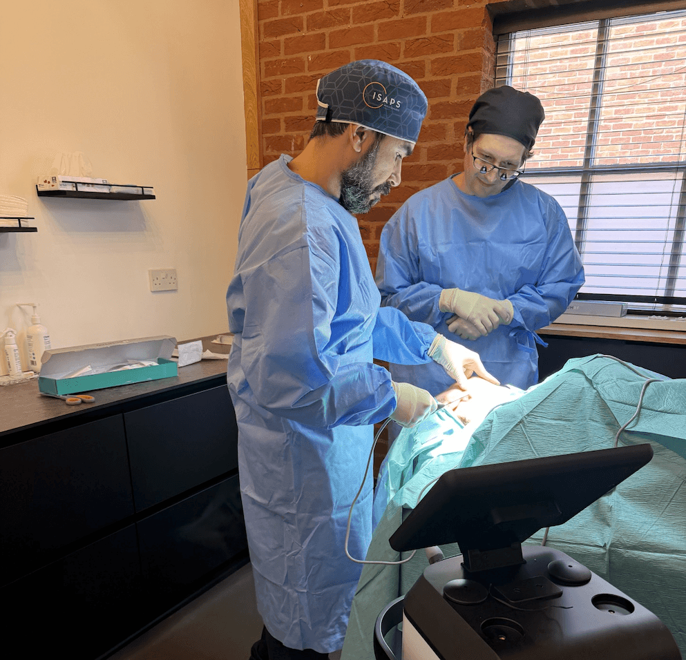 Two clinicians wearing surgical gowns and gloves during a procedure